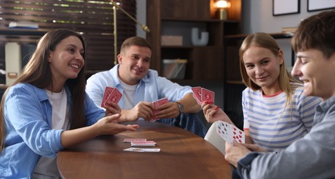 Photo of Group of friends playing cards at wooden table indoors