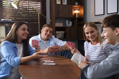 Photo of Group of friends playing cards at wooden table indoors