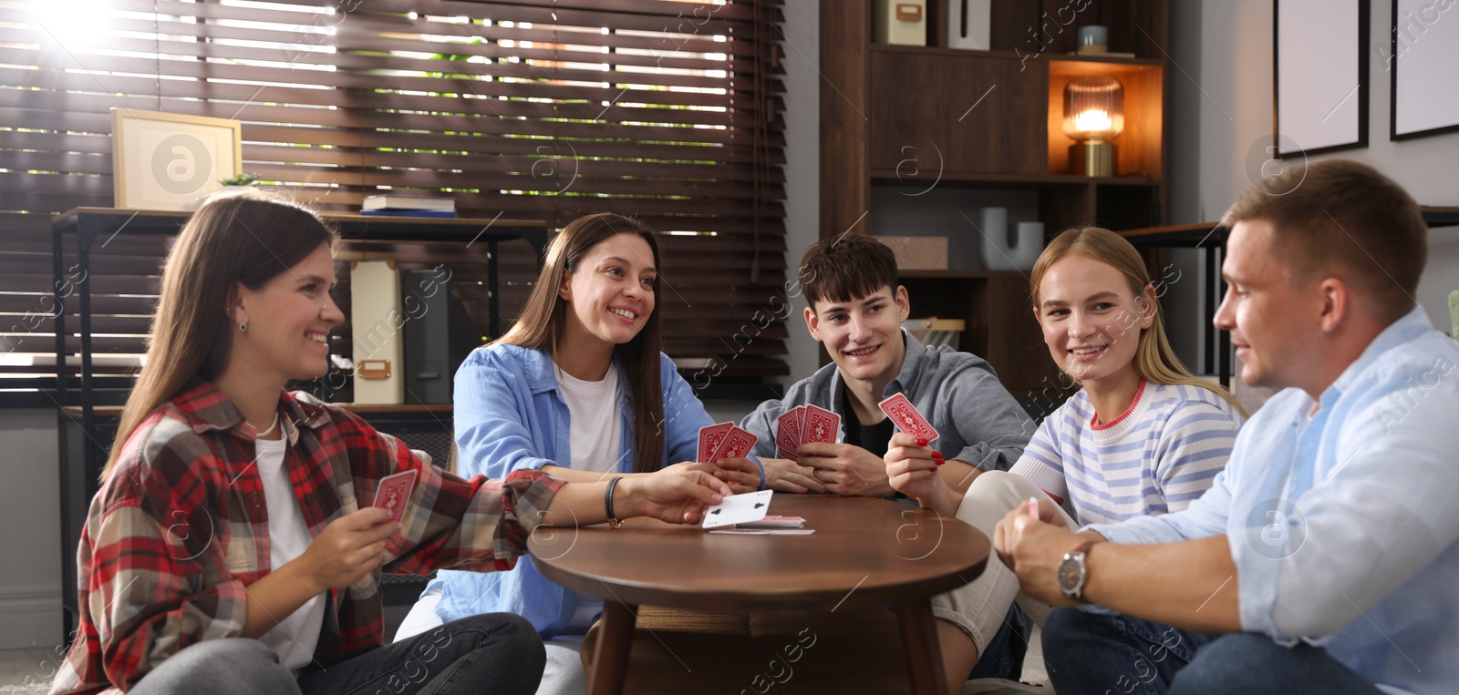 Photo of Group of friends playing cards at wooden table indoors