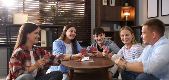 Photo of Group of friends playing cards at wooden table indoors