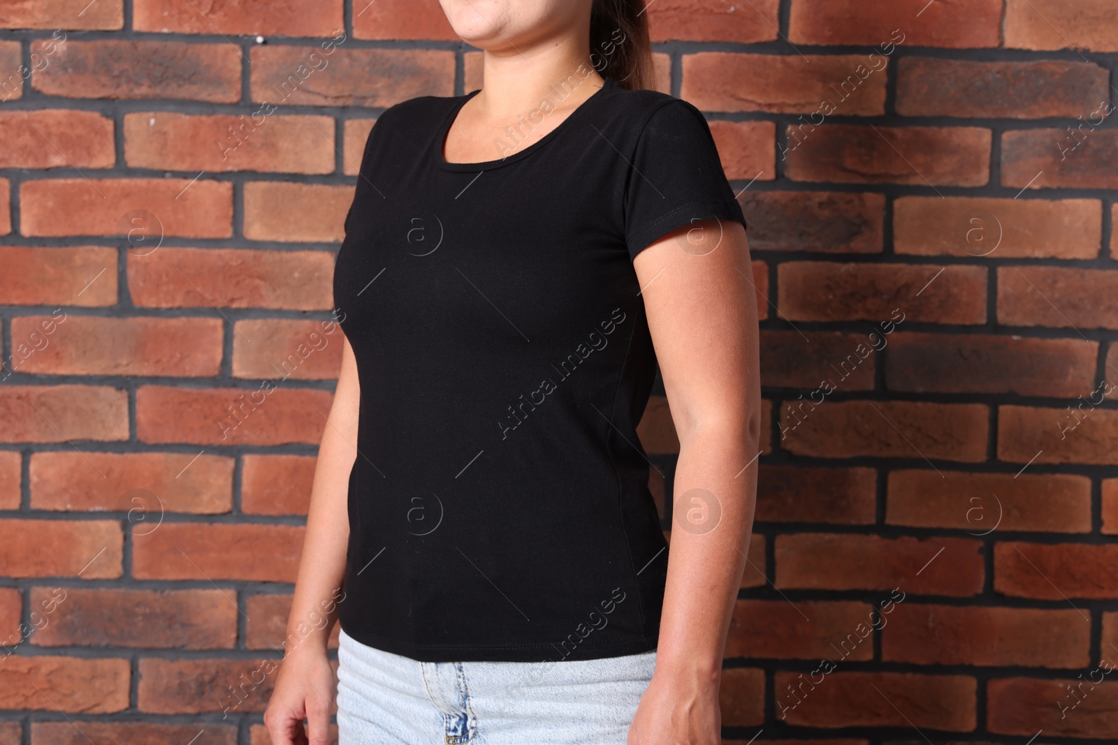 Photo of Young woman wearing stylish black t-shirt near brick wall, closeup. Mockup for design