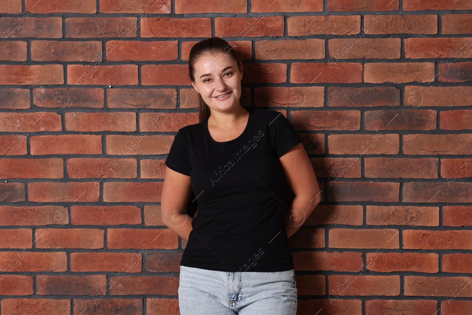 Photo of Young woman wearing stylish black t-shirt near brick wall. Mockup for design