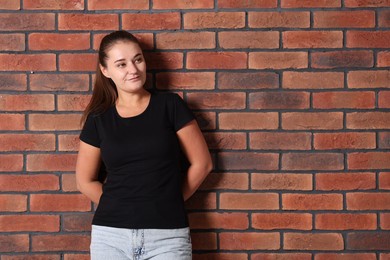 Photo of Young woman wearing stylish black t-shirt near brick wall. Mockup for design