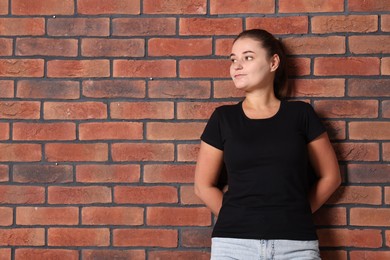 Photo of Young woman wearing stylish black t-shirt near brick wall. Mockup for design