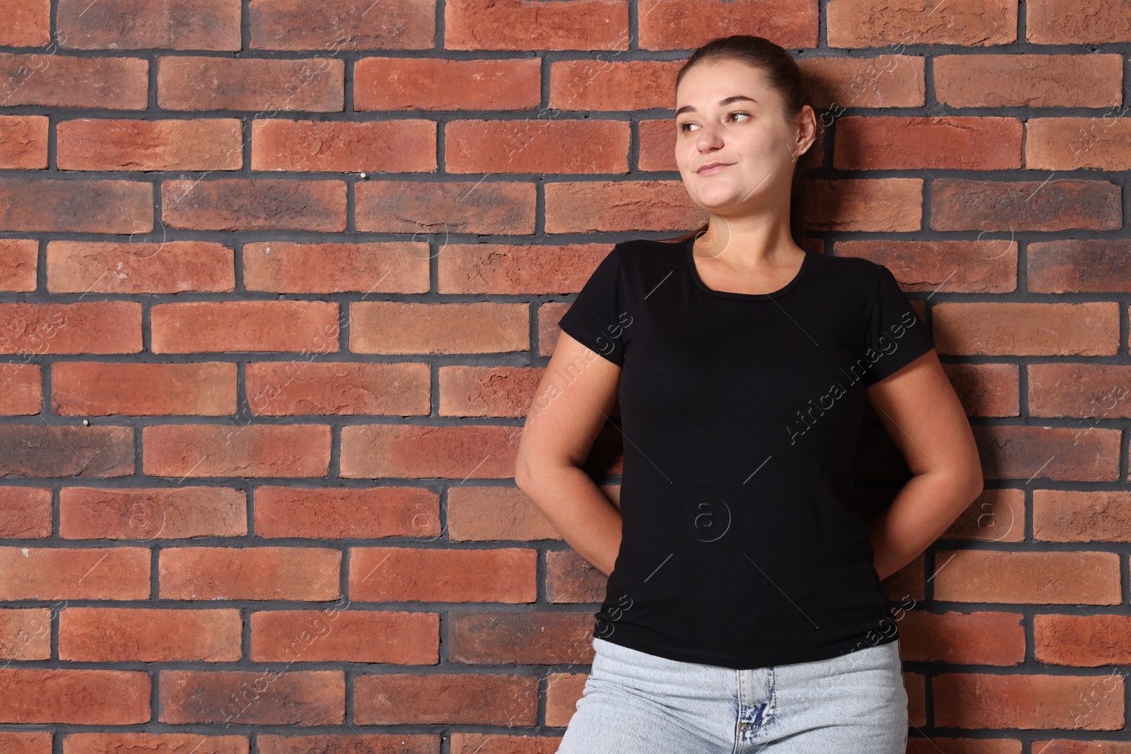 Photo of Young woman wearing stylish black t-shirt near brick wall. Mockup for design