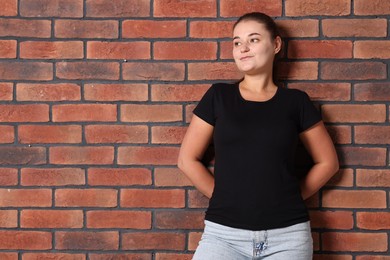 Photo of Young woman wearing stylish black t-shirt near brick wall. Mockup for design