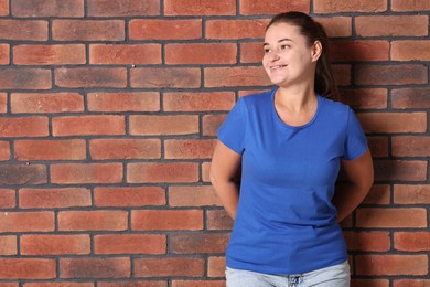 Photo of Young woman wearing stylish blue t-shirt near brick wall. Mockup for design