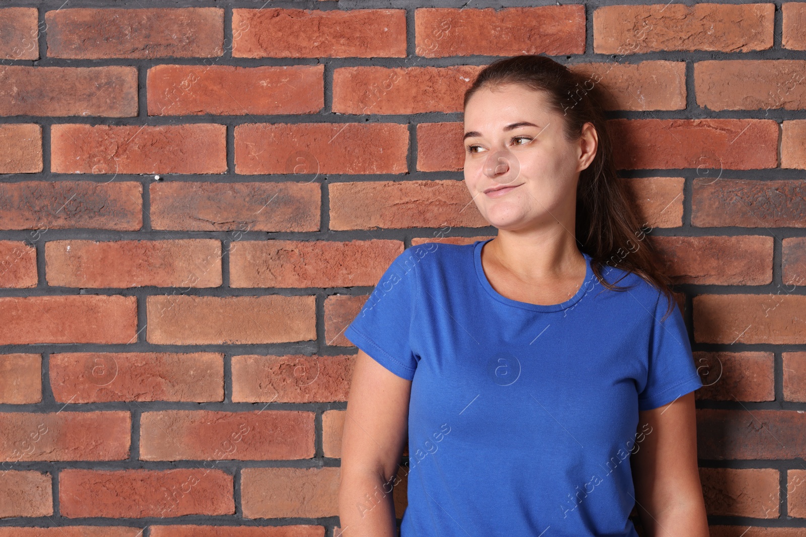 Photo of Young woman wearing stylish blue t-shirt near brick wall. Mockup for design