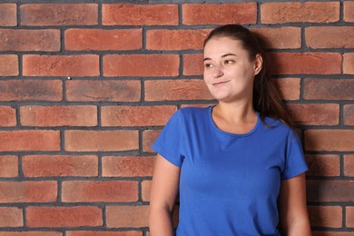 Photo of Young woman wearing stylish blue t-shirt near brick wall. Mockup for design