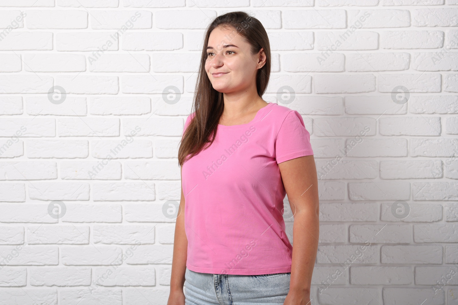 Photo of Young woman wearing stylish pink t-shirt near white brick wall. Mockup for design