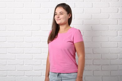 Photo of Young woman wearing stylish pink t-shirt near white brick wall. Mockup for design