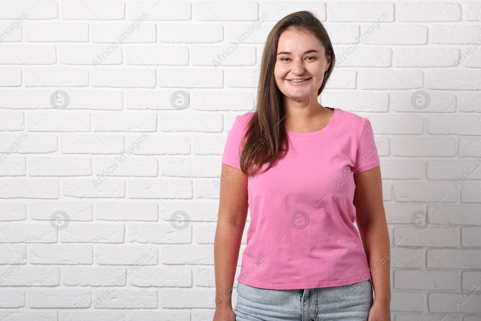 Photo of Young woman wearing stylish pink t-shirt near white brick wall. Mockup for design