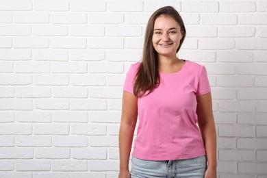 Photo of Young woman wearing stylish pink t-shirt near white brick wall. Mockup for design