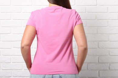Photo of Young woman wearing stylish pink t-shirt near white brick wall, back view. Mockup for design