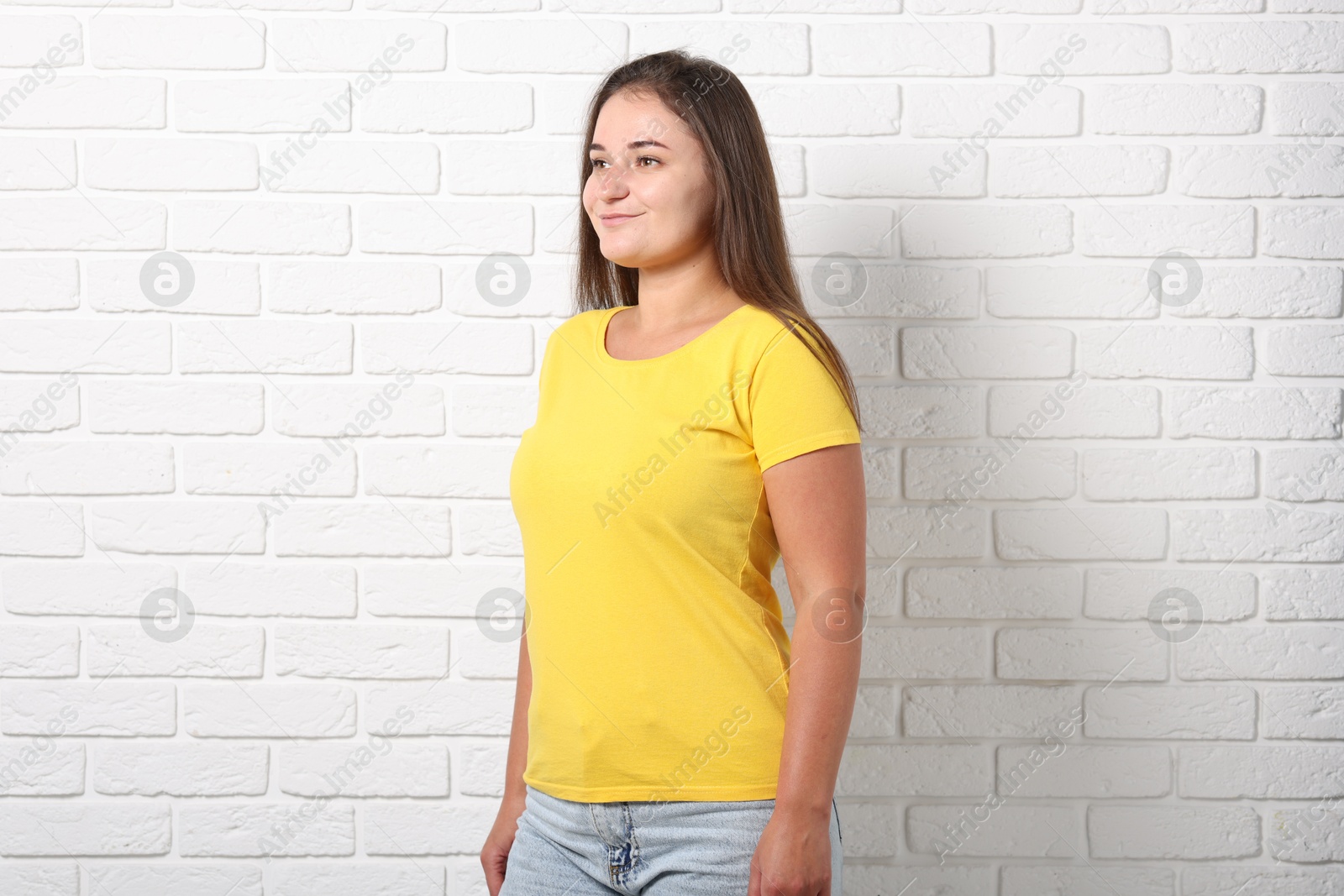 Photo of Young woman wearing stylish yellow t-shirt near white brick wall. Mockup for design