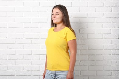 Photo of Young woman wearing stylish yellow t-shirt near white brick wall. Mockup for design