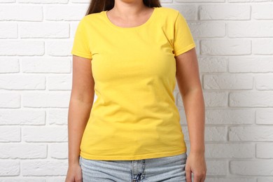 Photo of Young woman wearing stylish yellow t-shirt near white brick wall, closeup. Mockup for design