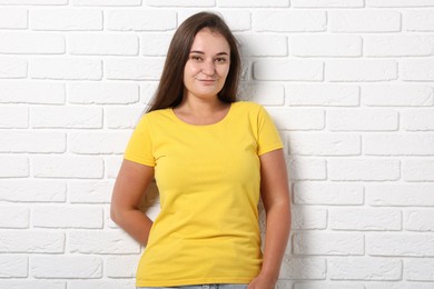 Photo of Young woman wearing stylish yellow t-shirt near white brick wall. Mockup for design
