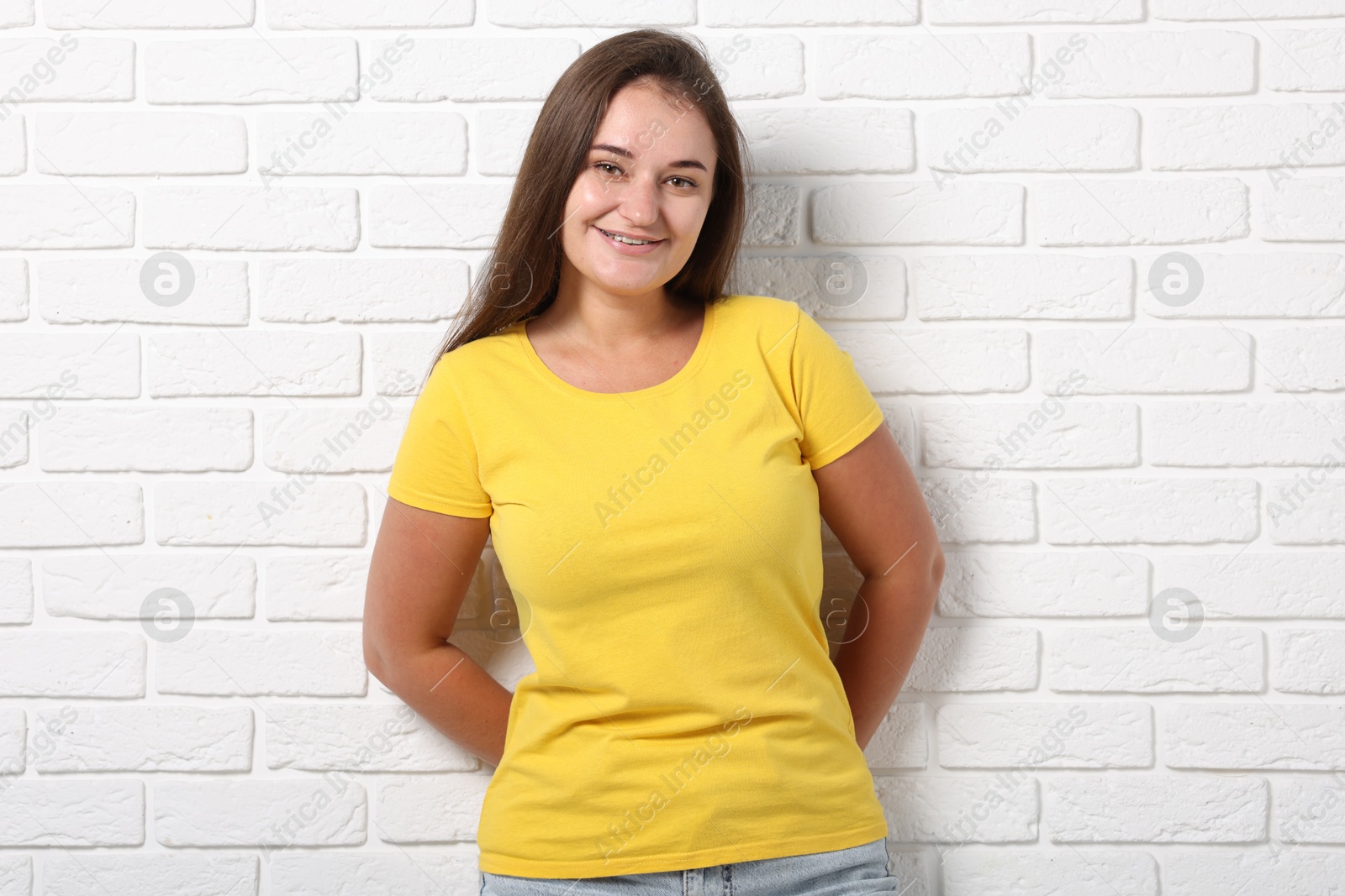 Photo of Young woman wearing stylish yellow t-shirt near white brick wall. Mockup for design