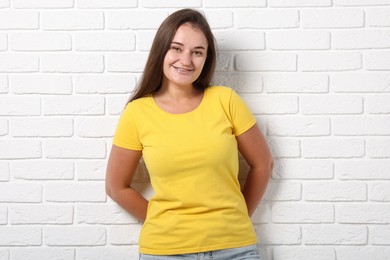 Photo of Young woman wearing stylish yellow t-shirt near white brick wall. Mockup for design