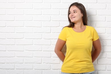 Photo of Young woman wearing stylish yellow t-shirt near white brick wall. Mockup for design