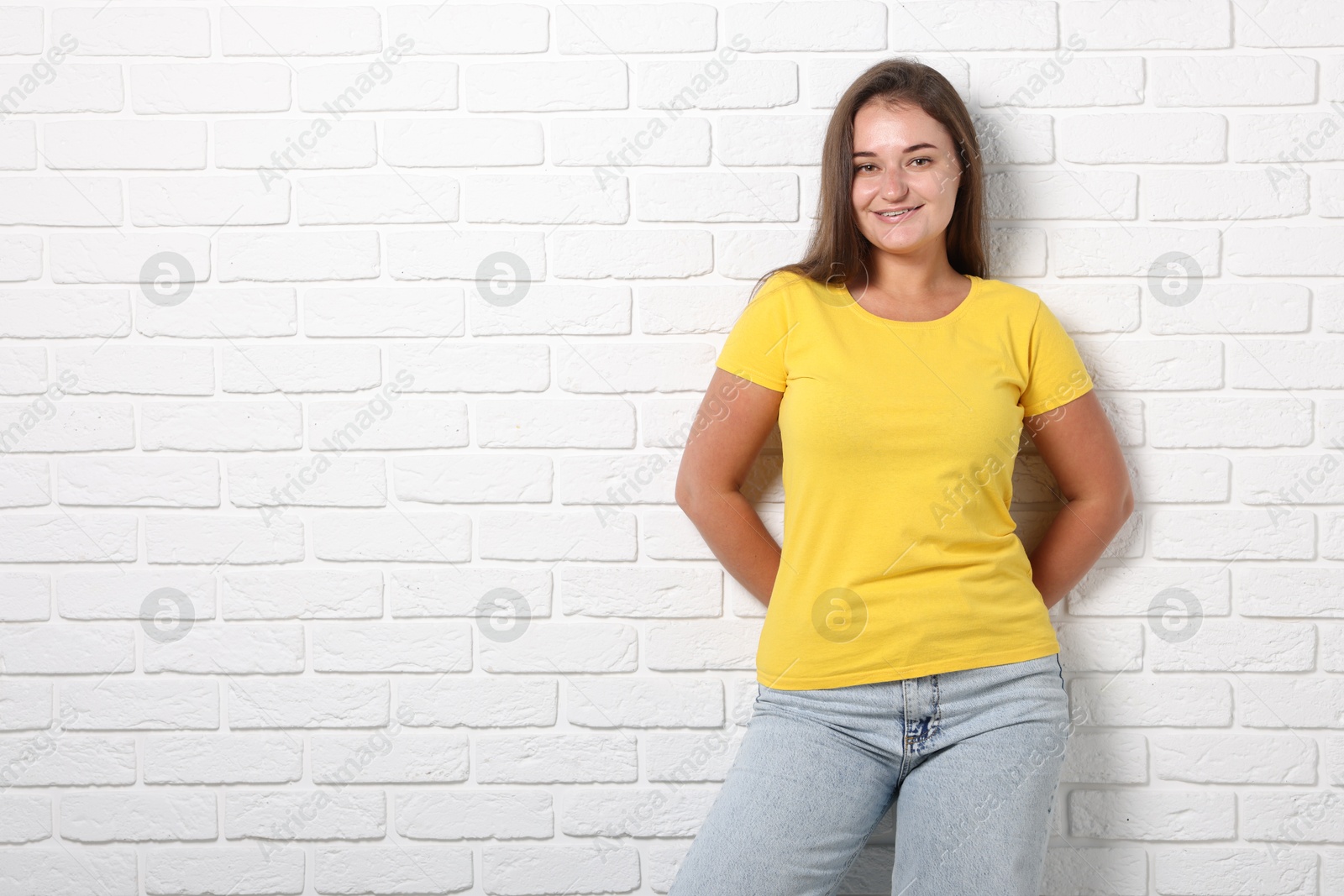 Photo of Young woman wearing stylish yellow t-shirt near white brick wall. Mockup for design
