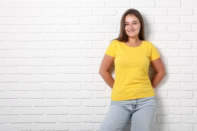 Photo of Young woman wearing stylish yellow t-shirt near white brick wall. Mockup for design