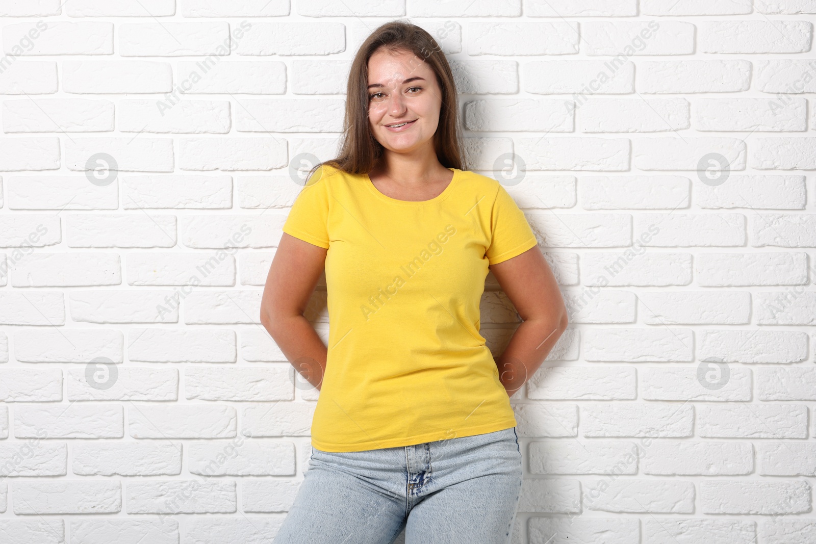Photo of Young woman wearing stylish yellow t-shirt near white brick wall. Mockup for design