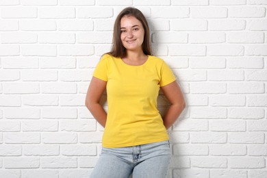 Photo of Young woman wearing stylish yellow t-shirt near white brick wall. Mockup for design