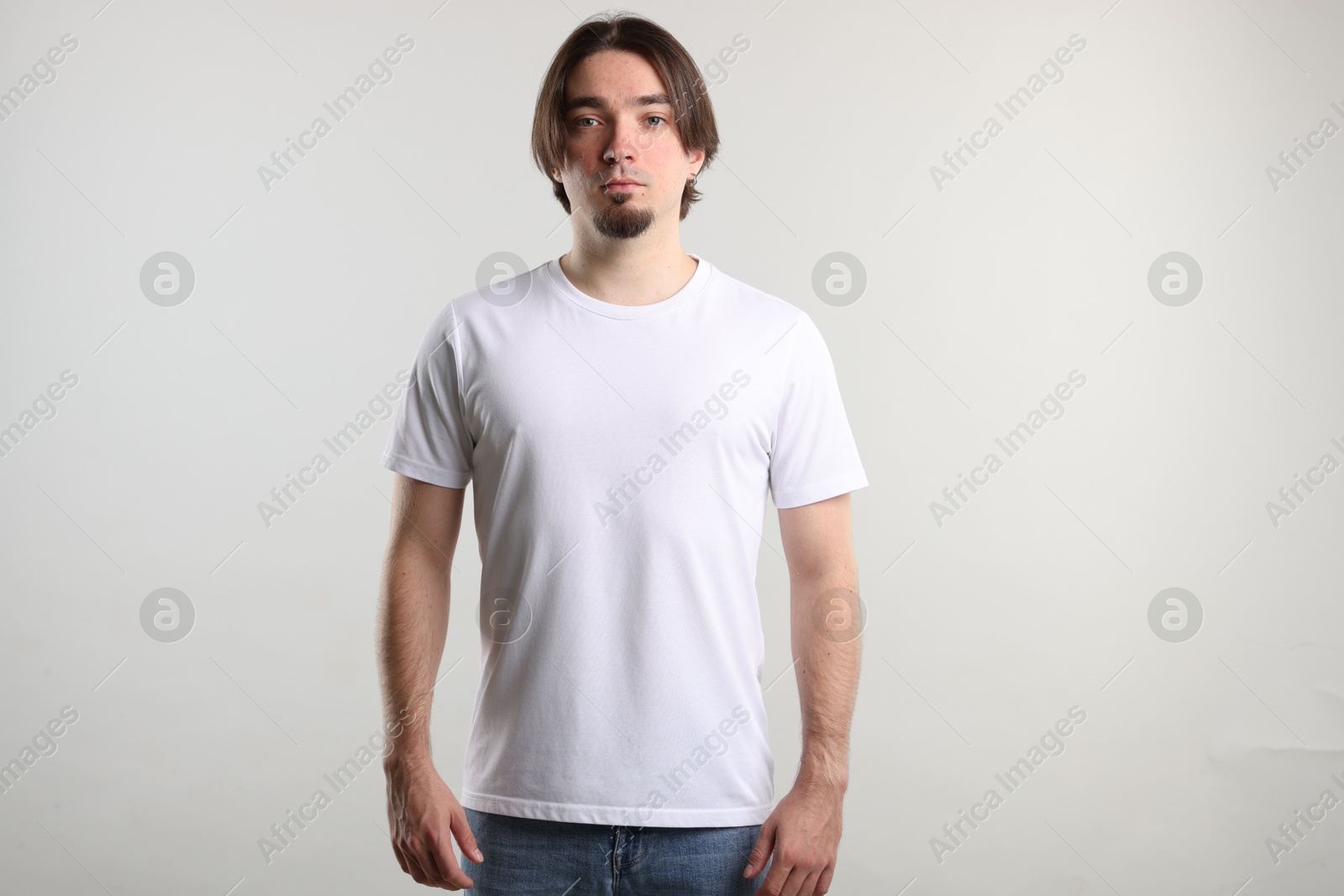 Photo of Young man wearing stylish white t-shirt near light grey background. Mockup for design
