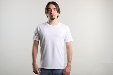 Photo of Young man wearing stylish white t-shirt near light grey background. Mockup for design