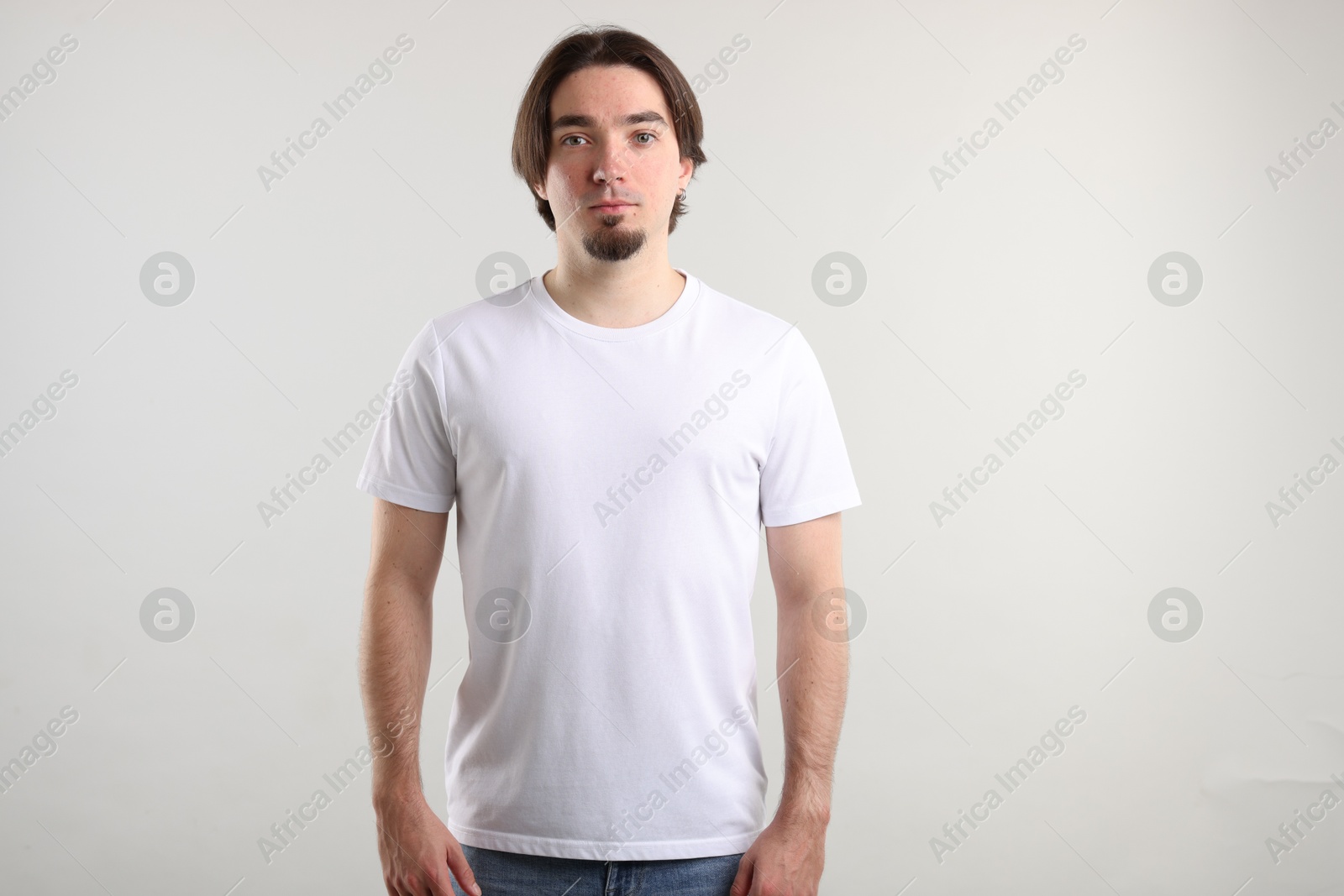 Photo of Young man wearing stylish white t-shirt near light grey background. Mockup for design
