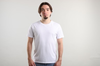 Photo of Young man wearing stylish white t-shirt near light grey background. Mockup for design