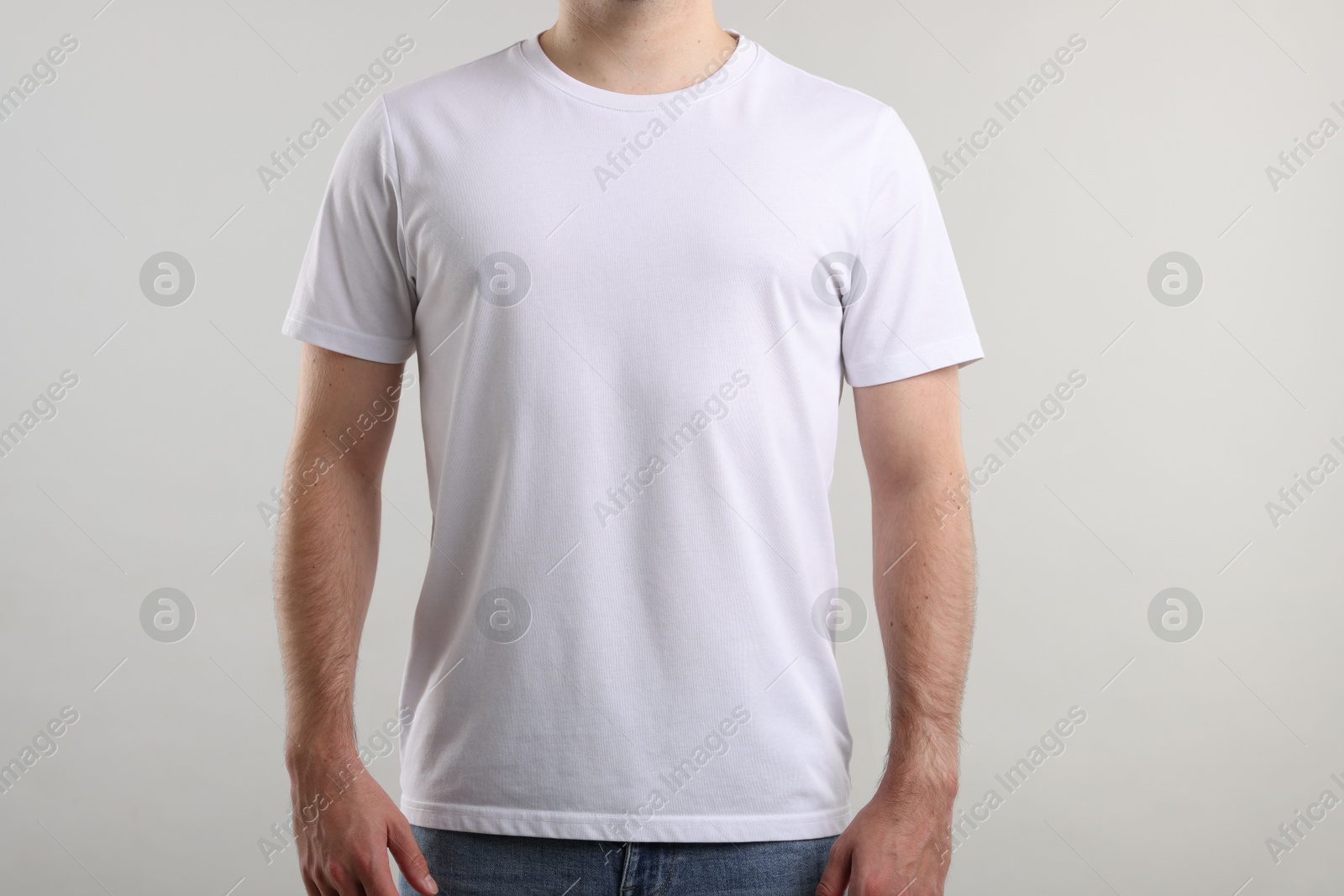 Photo of Young man wearing stylish white t-shirt near light grey background, closeup. Mockup for design