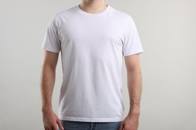 Photo of Young man wearing stylish white t-shirt near light grey background, closeup. Mockup for design