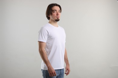 Photo of Young man wearing stylish white t-shirt near light grey background. Mockup for design