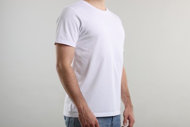 Photo of Young man wearing stylish white t-shirt near light grey background, closeup. Mockup for design