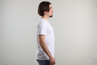 Photo of Young man wearing stylish white t-shirt near light grey background. Mockup for design