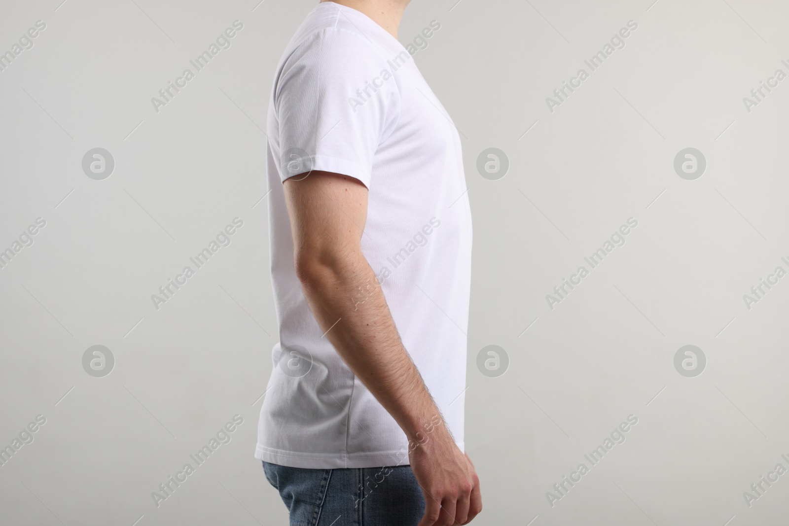 Photo of Young man wearing stylish white t-shirt near light grey background, closeup. Mockup for design
