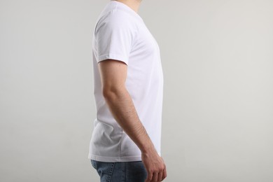Photo of Young man wearing stylish white t-shirt near light grey background, closeup. Mockup for design
