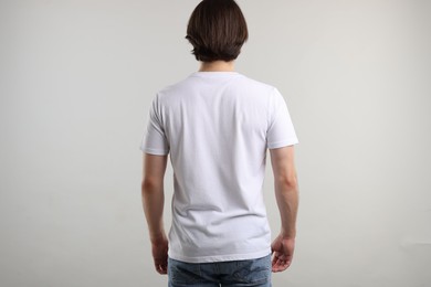 Photo of Young man wearing stylish white t-shirt near light grey background, back view. Mockup for design