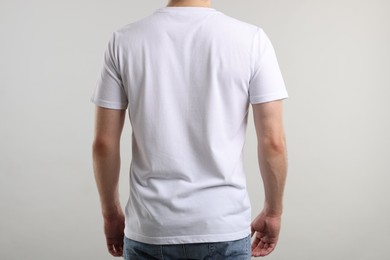Photo of Young man wearing stylish white t-shirt near light grey background, back view. Mockup for design