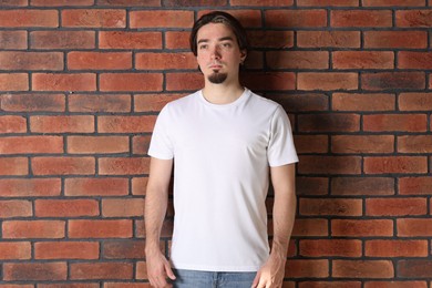 Photo of Young man wearing stylish white t-shirt near brick wall. Mockup for design