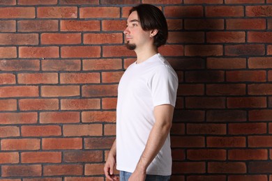 Photo of Young man wearing stylish white t-shirt near brick wall. Mockup for design