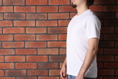 Photo of Young man wearing stylish white t-shirt near brick wall, closeup. Mockup for design