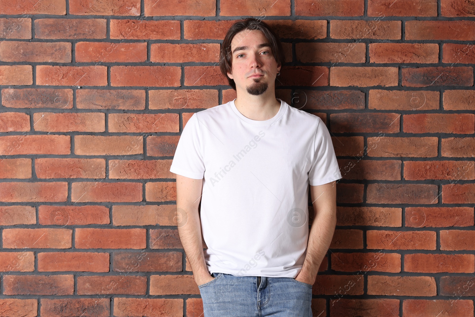Photo of Young man wearing stylish white t-shirt near brick wall. Mockup for design