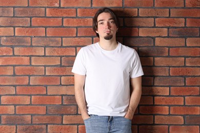 Photo of Young man wearing stylish white t-shirt near brick wall. Mockup for design