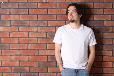 Photo of Young man wearing stylish white t-shirt near brick wall. Mockup for design