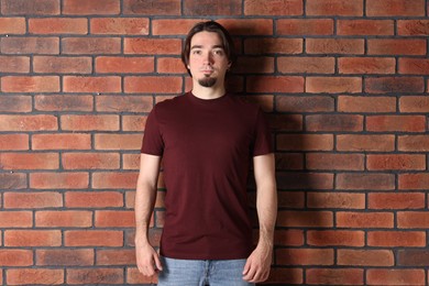 Photo of Young man wearing stylish brown t-shirt near brick wall. Mockup for design