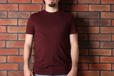 Photo of Young man wearing stylish brown t-shirt near brick wall, closeup. Mockup for design